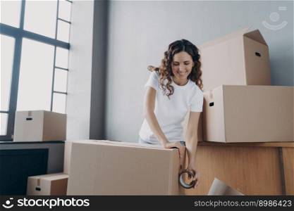 Happy girl moves alone. Young woman is packing boxes with adhesive tape. Lady is wrapping cardboard boxes with packing tape. Moving service worker preparing boxes for shipping and storage.. Happy girl moves alone. Young woman is packing boxes with adhesive tape for shipping.