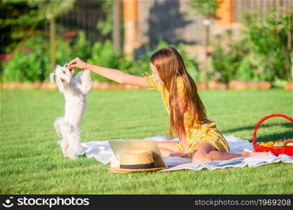Happy girl on picnic playing with white puppy on green grass in the park. Two little kids on picnic in the park