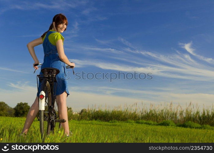 Happy girl over a bicycle and looking back, in a green meadow