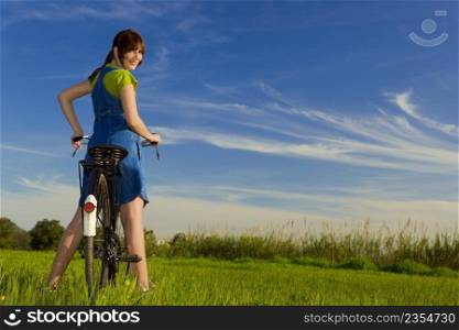 Happy girl over a bicycle and looking back, in a green meadow