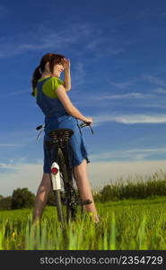 Happy girl over a bicycle and looking the view, in a green meadow