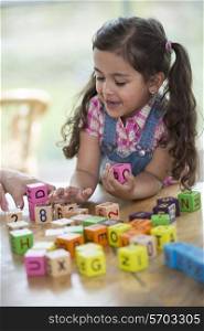 Happy girl playing with alphabet blocks at table