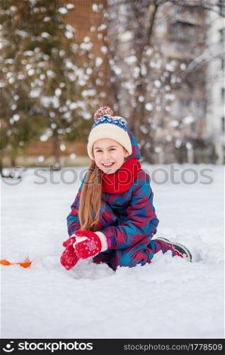 Happy girl playing with snow on a snowy winter walk, making snowballs in the park. Winter outdoor games.. Happy girl playing with snow on a snowy winter walk, making snowballs in the park.