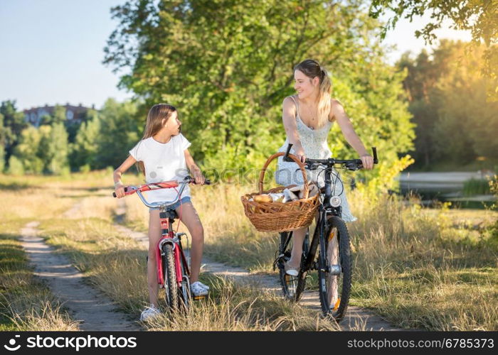 Happy girl riding on bicycle with her mother in meadow at sunset