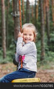 Happy girl riding on the zip line in rope park in forest while spending summer vacation. Real people, authentic situations