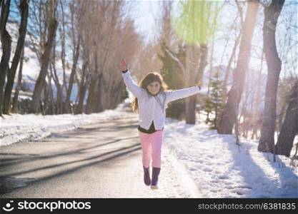 Happy girl runs and jumps up from happiness, beautiful smiling schoolgirl with raised up hands enjoying warm sunny weather in wintertime park, happy winter holidays, baby in good health embrasing life, wellness concept