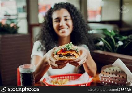Happy girl showing burger in a restaurant. Close-up of a girl showing appetizing hamburger in a restaurant