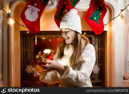 Happy girl sitting at fireplace and looking at gift in box