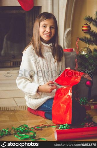 Happy girl sitting at fireplace and wrapping Christmas presents