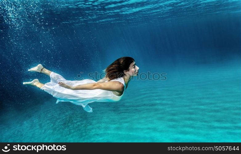 Happy girl swimming underwater, wearing stylish dress, luxury sea performance, active summer vacation, relaxation and enjoyment concept