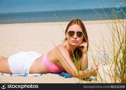 Happy girl taking selfie photo on beach.. Fun and joy. Summer time. Young beauty girl spending time on beach taking selfie photo by mobile phone. Positive woman with smartphone lying on blanket.