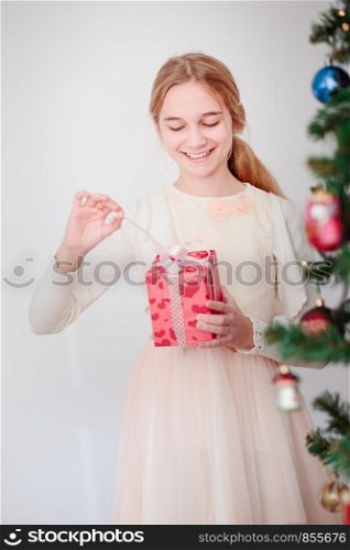 Happy girl unpacking Christmas gift standing behind a tree