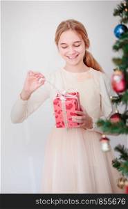 Happy girl unpacking Christmas gift standing behind a tree