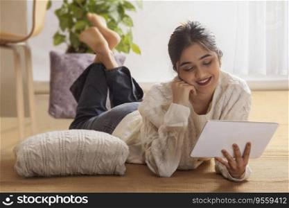 Happy girl using digital tablet while lying down on floor
