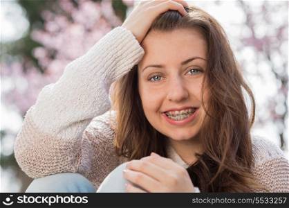 Happy girl wearing braces with hand in hair outdoors spring