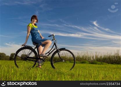 Happy girl with a bicycle in a green meadow