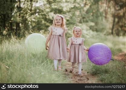 Happy girl with balloons. two beautiful little girls in the summer in a park with balloons in hands. two beautiful little girls in the summer in a park with balloons in hands. Happy girl with balloons.