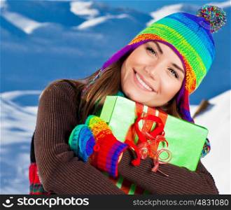 Happy girl with Christmas gift, winter outdoor portrait, beautiful female teen wearing colorful hat, young pretty smiling woman, holding present box in hands