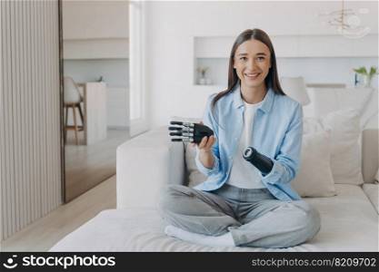 Happy girl with disability enjoying using modern lightweight high tech bionic prosthesis of arm, sitting on sofa at home. Smiling disabled woman showing how to disassemble artificial limb.. Happy girl with disability enjoying using bionic prosthesis of arm, sitting on sofa at home