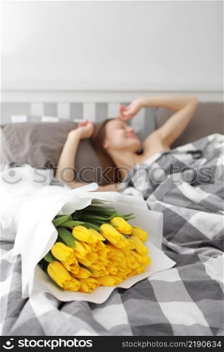 happy Girl with flowers yellow tulips lying on a bed with enjoying flowers and romantic gift in Valentine day. She just woken up and have presented her a bouquet of flowers. A birthday, woman&rsquo;s day. happy Girl with flowers yellow tulips lying on a bed with enjoying flowers and romantic gift in Valentine day. She just woken up and have presented her a bouquet of flowers. A birthday, woman&rsquo;s day,