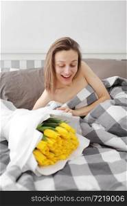 happy Girl with flowers yellow tulips lying on a bed with enjoying flowers and romantic gift in Valentine day. She just woken up and have presented her a bouquet of flowers. A birthday, woman&rsquo;s day. happy Girl with flowers yellow tulips lying on a bed with enjoying flowers and romantic gift in Valentine day. She just woken up and have presented her a bouquet of flowers. A birthday, woman&rsquo;s day,