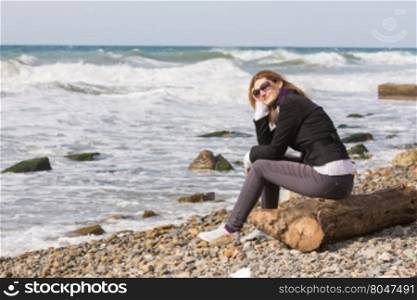 Happy girl with glasses sitting on a log on a rocky beach ocean