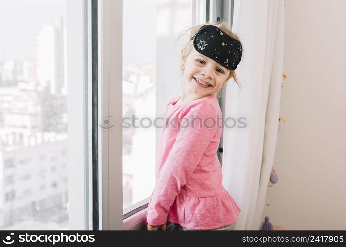 happy girl with sleeping eye mask standing near glass window