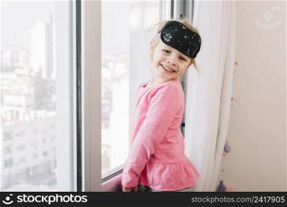 happy girl with sleeping eye mask standing near glass window