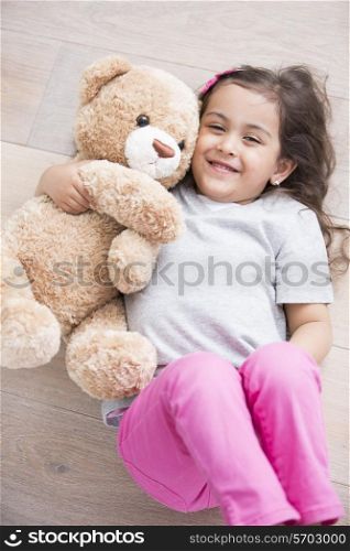 Happy girl with teddy bear lying on wooden floor at home