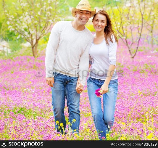 Happy girlfriend and boyfriend holding hands and walking on pink floral field, enjoying family, romantic relationship concept