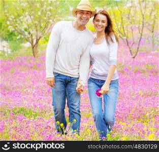 Happy girlfriend and boyfriend holding hands and walking on pink floral field, enjoying family, romantic relationship concept