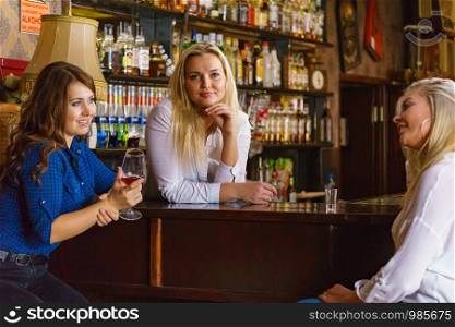 Happy girls best friends drinking alcohol in night club, gossiping and talking at counter with bar employee.. Girls in pub club gossiping and talking