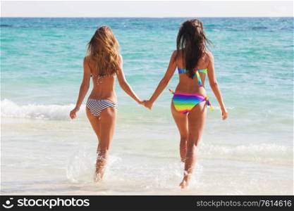 Happy girls running through the water at the beach, female friends, vacation fun. Happy girls running through the water