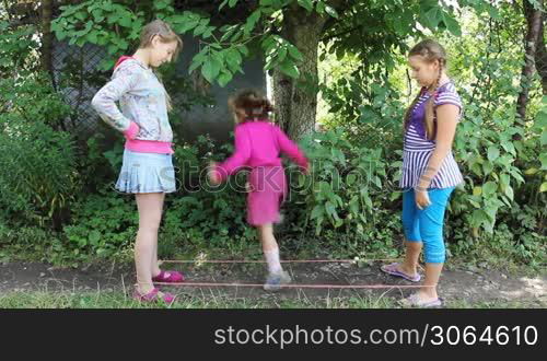 happy girls stand with rubber band stretched between them and little sister jumps through it, part2