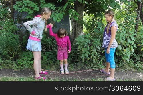 happy girls stand with rubber band stretched between them, and older sister teaches little girl jumping through it, part1