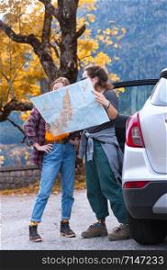 happy girls travel by car. Road trip - tourist girls with a map is standing near the car. Austria