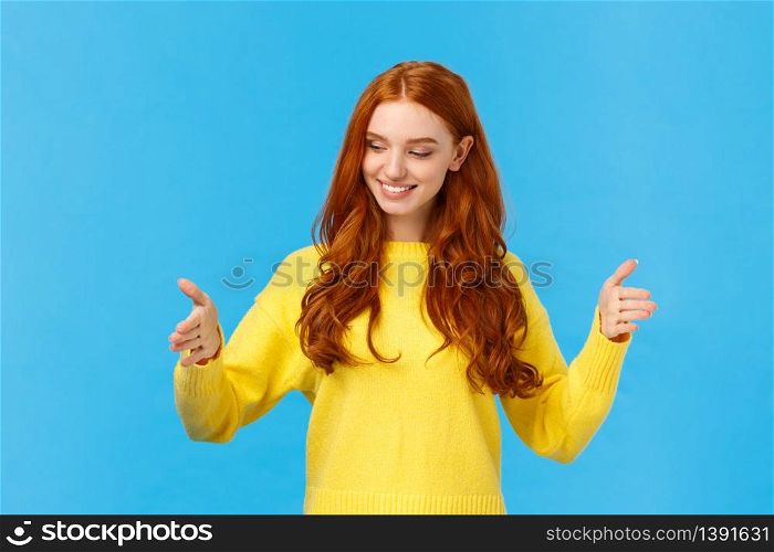 Happy good-looking young woman with red curly hair, freckles, shaping long object as if holding box over chest, looking satisfied, pleased with size, explain how big was gift, blue background.. Happy good-looking young woman with red curly hair, freckles, shaping long object as if holding box over chest, looking satisfied, pleased with size, explain how big was gift, blue background