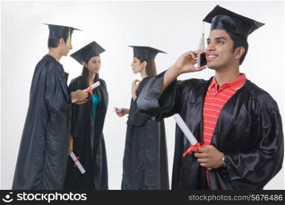 Happy graduate student answering smart phone with friends discussing against white background
