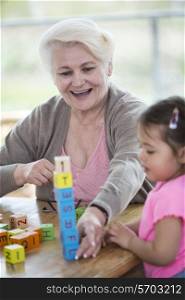 Happy grandmother and granddaughter playing with alphabet blocks in house