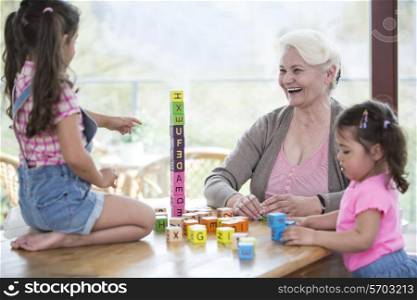Happy grandmother and granddaughters playing with alphabet blocks at table