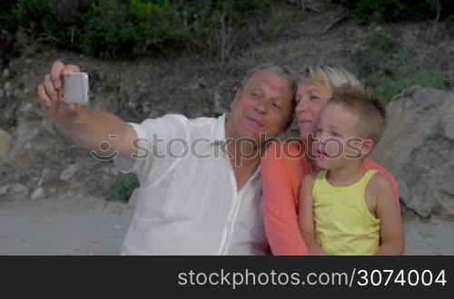 Happy grandmother, grandfather and grandchild taking selfie with smart phone outdoor. Family shot as mementos