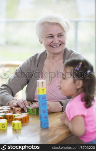 Happy grandmother looking away while granddaughter blowing stacked alphabet blocks in house