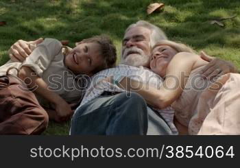 Happy grandpa and grandma with grandson playing and lying on grass in park. Slow motion