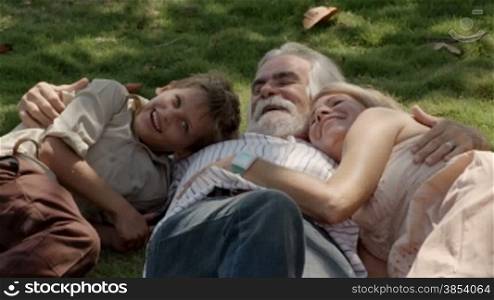 Happy grandpa and grandma with grandson playing and lying on grass in park. Slow motion