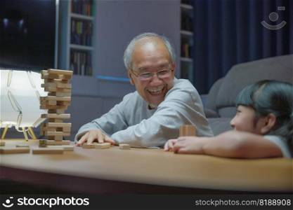 Happy grandparents Asian family enjoy playing toy block with little daughter and mother together at home night time, Smiling parent having fun play build constructor tower of wooden blocks, education