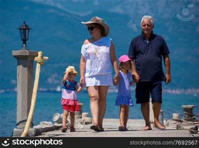 happy grandparents with cute little granddaughters having fun holding their hands while walking  by the sea during Summer vacation  Healthy family holiday concept