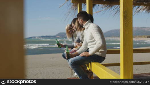 Happy Group Of Friends Hanging Out At Beach House having fun and drinking beer on autumn day