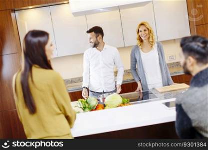 Happy group of young men and women cooking together at home in modern kitchen