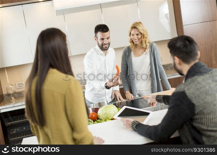 Happy group of young  men and women cooking together at home in modern kitchen