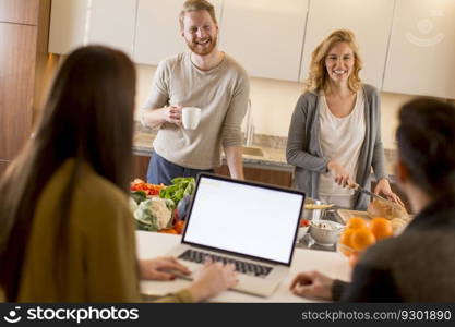 Happy group of young men and women cooking together at home in modern kitchen